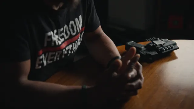 Devin Perkins' holstered pistol on the table as he talks with the filmmakers.