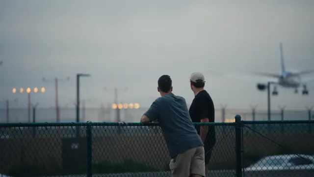 Josh and Tommy lean on the airport fence near LAX to watch a jet come in to land.